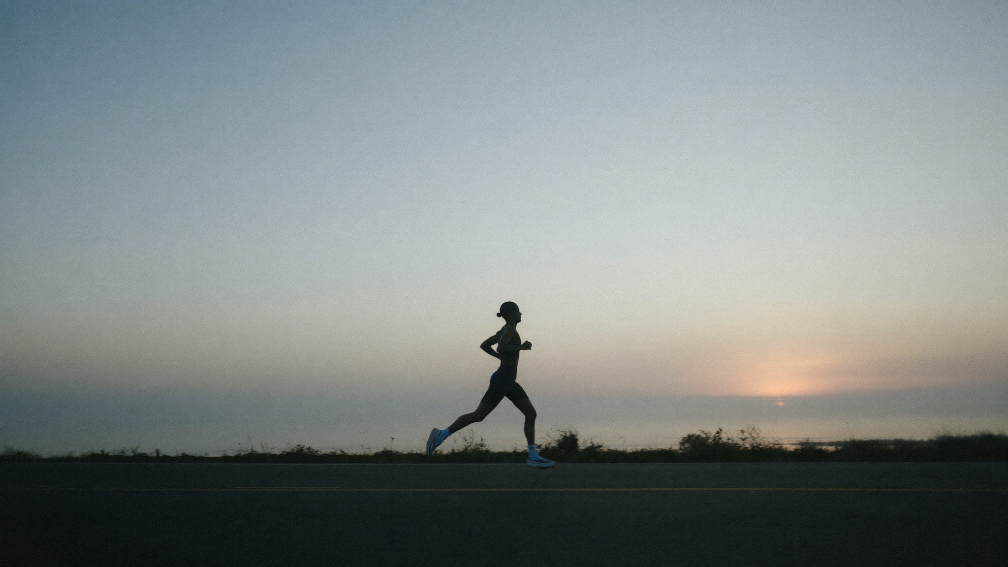 A runner on a coastal road at a magenta sunrise